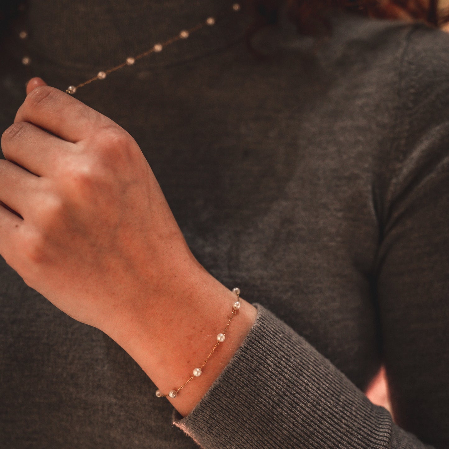 Person wearing a dark gray sweater with a bracelet on a neutral background
