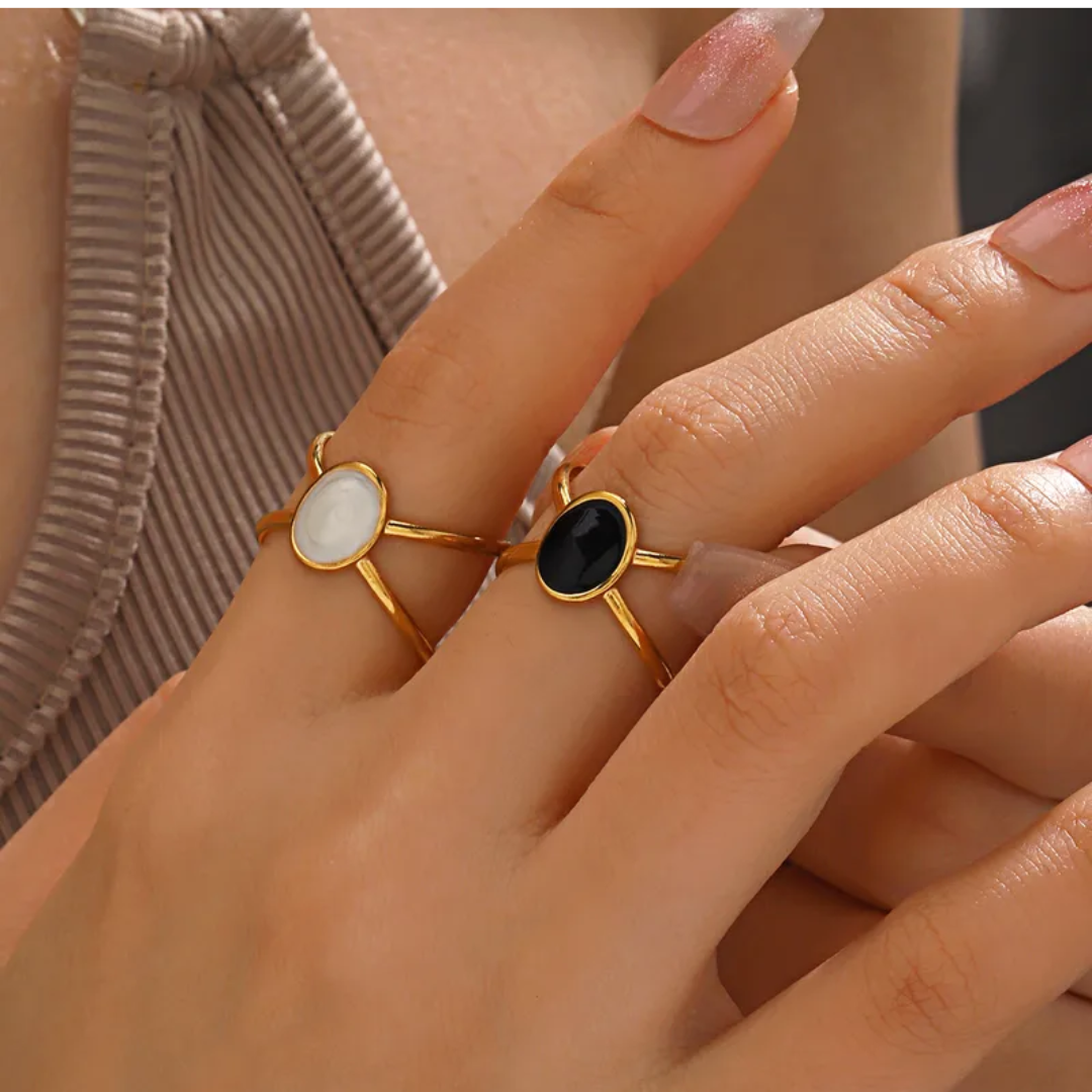 Close-up of a hand wearing two gold rings with gemstones on a neutral background