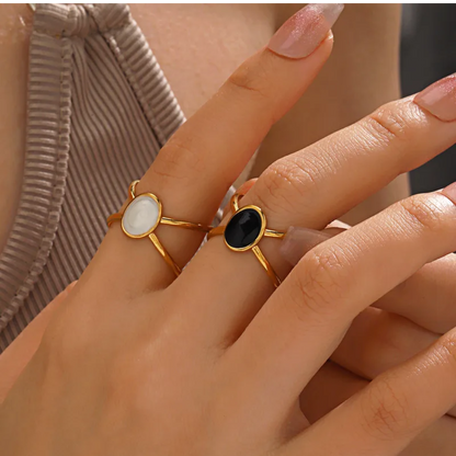Close-up of a hand wearing two gold rings with gemstones on a neutral background