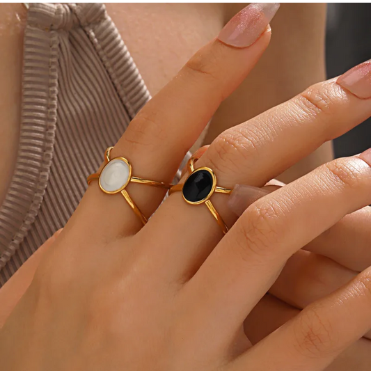 Close-up of a hand wearing two gold rings with gemstones on a neutral background