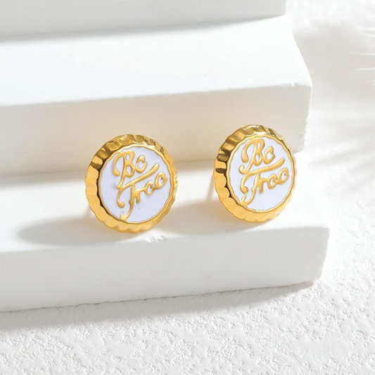 Gold and white earrings with 'Be Free' inscription on a white surface