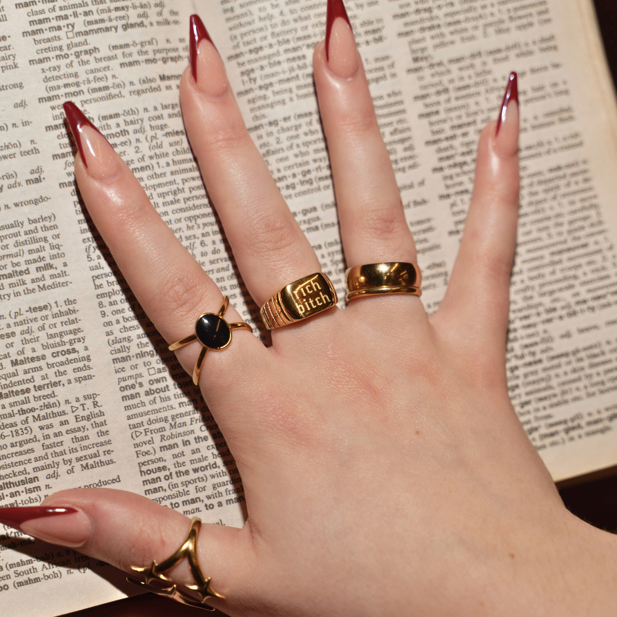 Hand wearing multiple gold rings on a textured surface