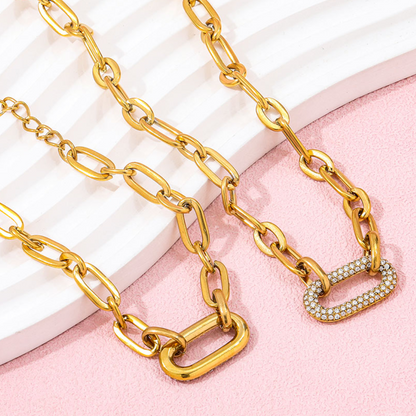 Gold chain necklace with a heart-shaped clasp on a pink and white background