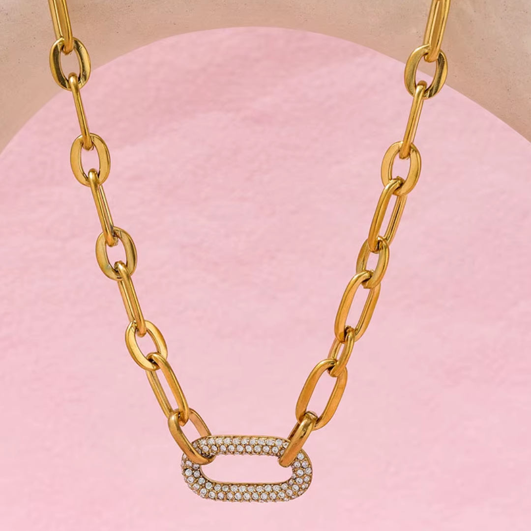 Gold chain necklace with a diamond pendant on a pink background