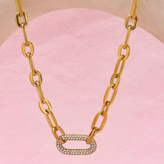 Gold chain necklace with a diamond pendant on a pink background