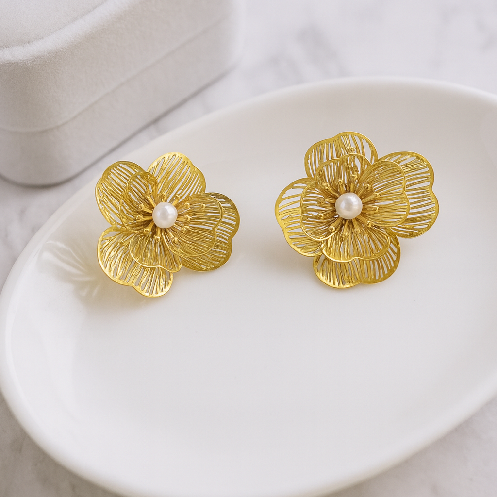 Gold floral earrings with pearl centers on a white dish.