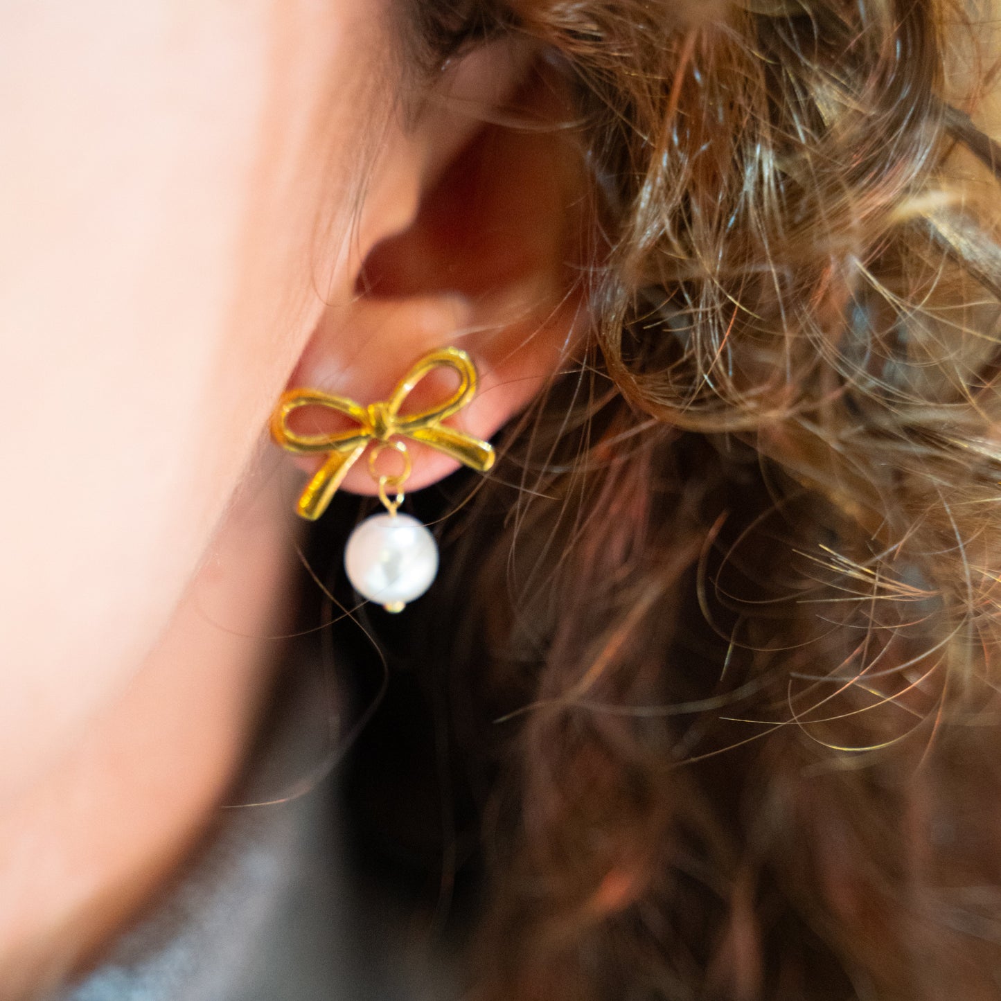 Close-up of an ear wearing a gold bow and pearl earring.