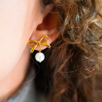 Close-up of an ear wearing a gold bow and pearl earring.