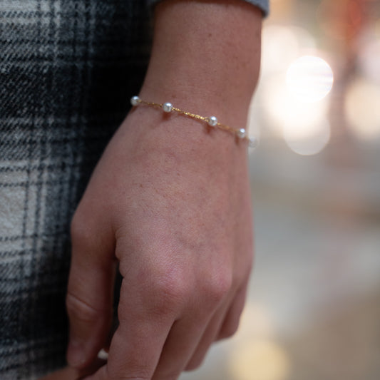 Hand wearing a pearl bracelet with a blurred background