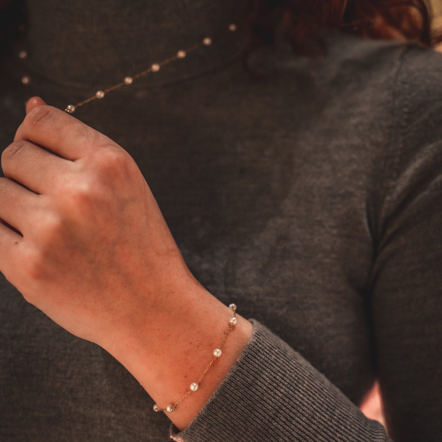 Person wearing a dark gray sweater with a bracelet on a neutral background