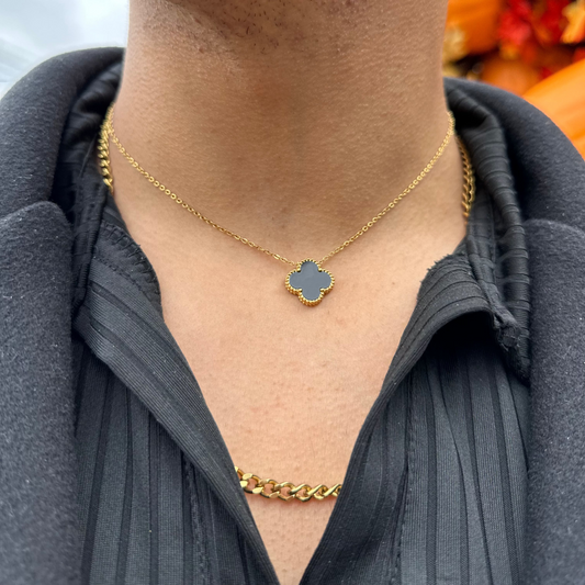 Person wearing a gold necklace with a clover-shaped pendant.