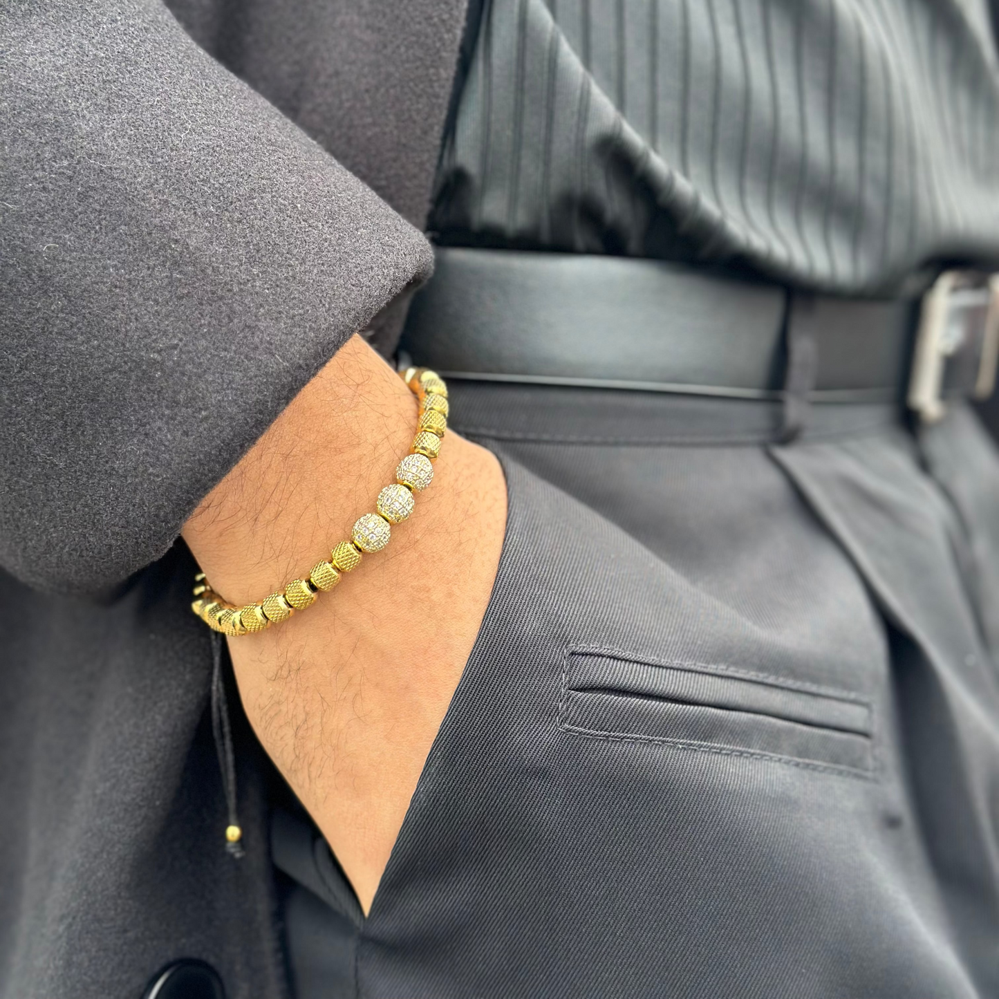 Person wearing a gray coat with a gold bracelet on a neutral background