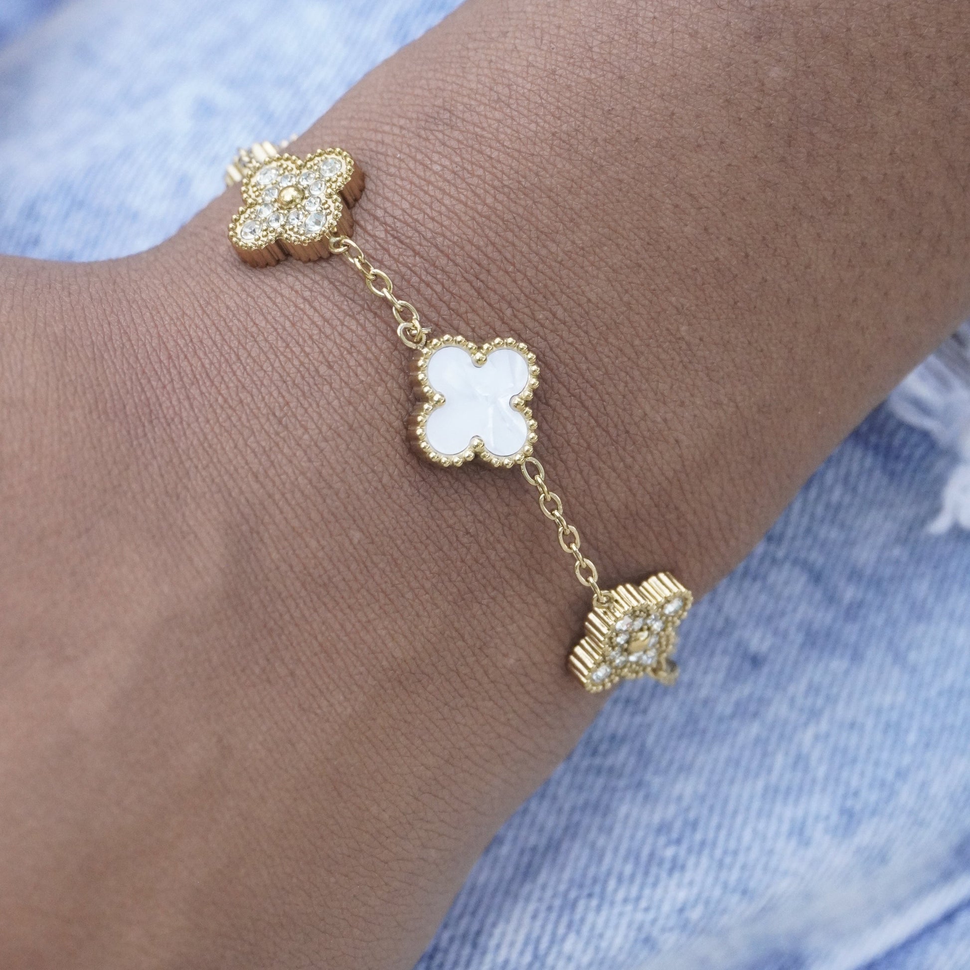 Gold bracelet with clover-shaped charms on a wrist against a denim background