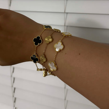 Wrist wearing multiple gold bracelets with clover-shaped charms against a white background
