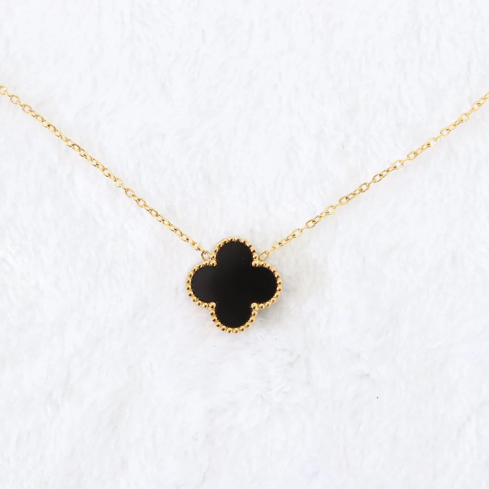 Black clover-shaped pendant on a gold chain against a white background