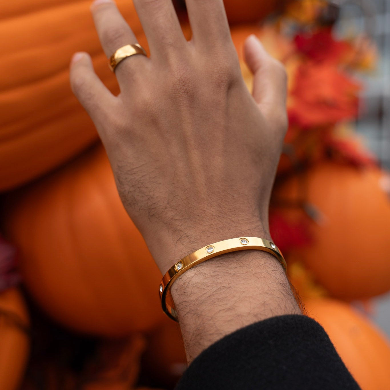 Hand with gold ring and bracelet against a blurred background of pumpkins