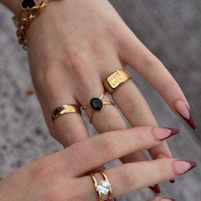 Close-up of a hand wearing multiple gold rings and bracelets on a blurred background