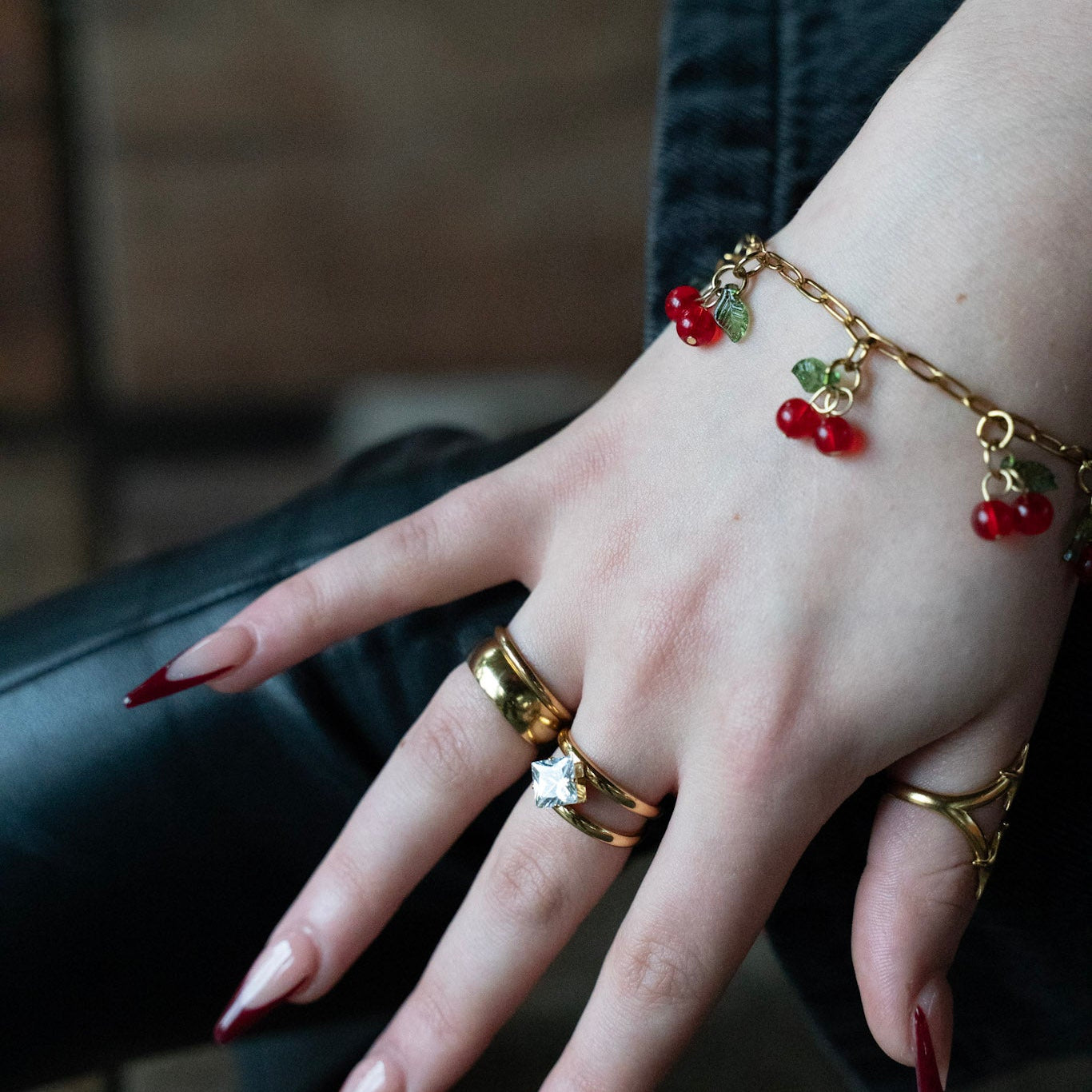 Hand wearing gold rings and a bracelet with red berries against a blurred background