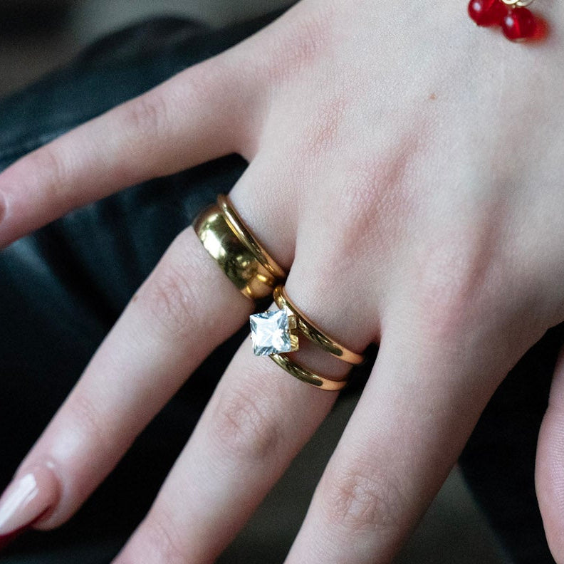 Hand wearing gold rings and a bracelet with red berries against a blurred background