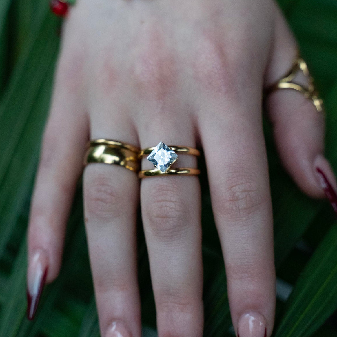 Hand with gold rings and a bracelet on a green leaf background
