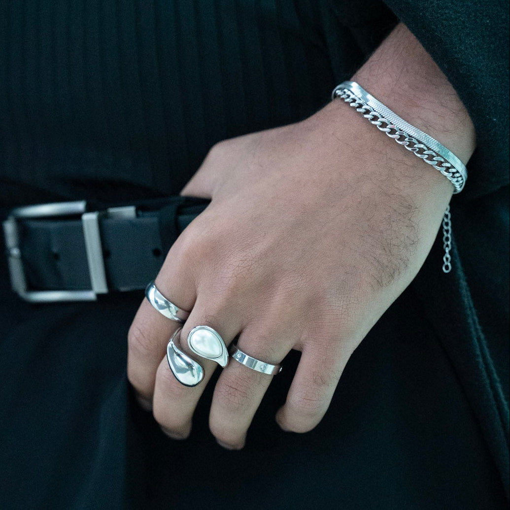 Person wearing multiple silver rings on a dark background