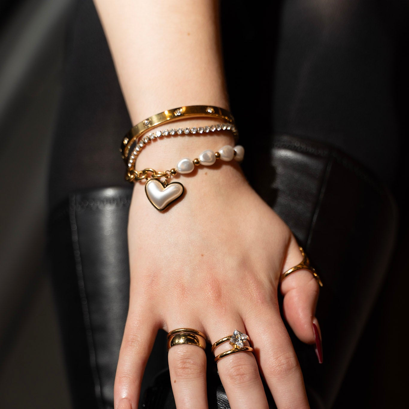 Hand wearing multiple gold rings and bracelets on a dark background