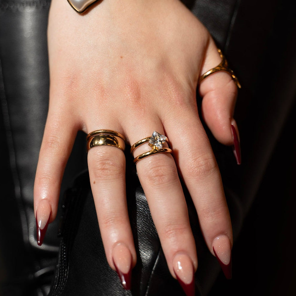 Hand wearing multiple gold rings and bracelets on a dark background
