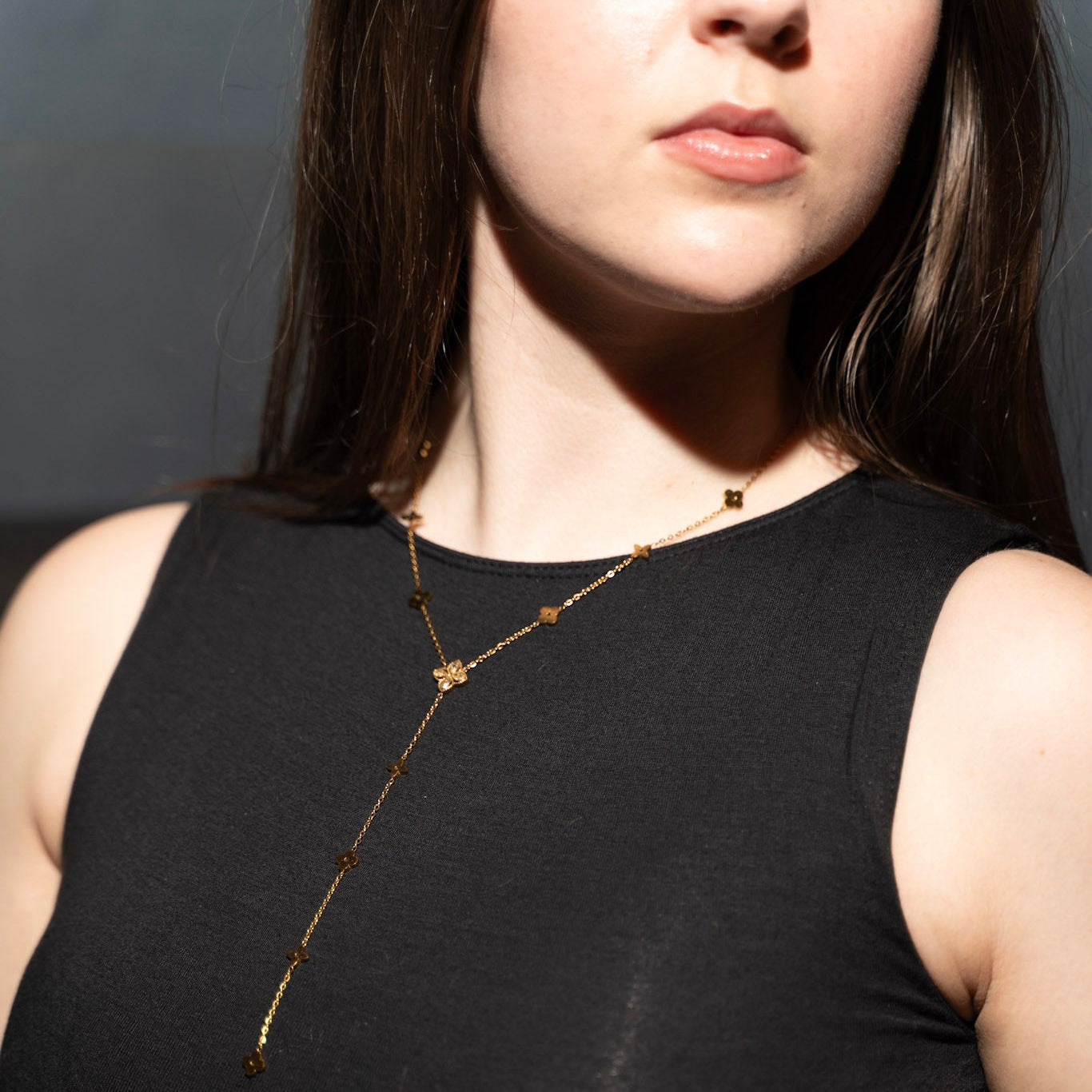 Woman wearing a black sleeveless top with a long necklace against a dark background