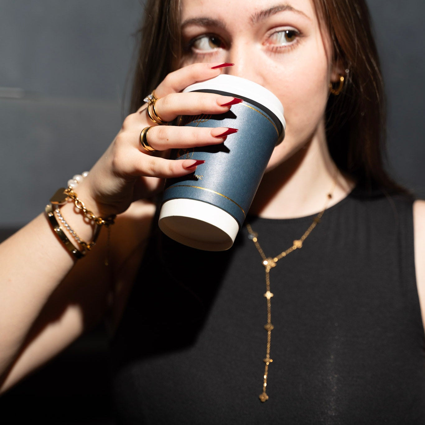 Woman drinking from a paper cup against a dark background