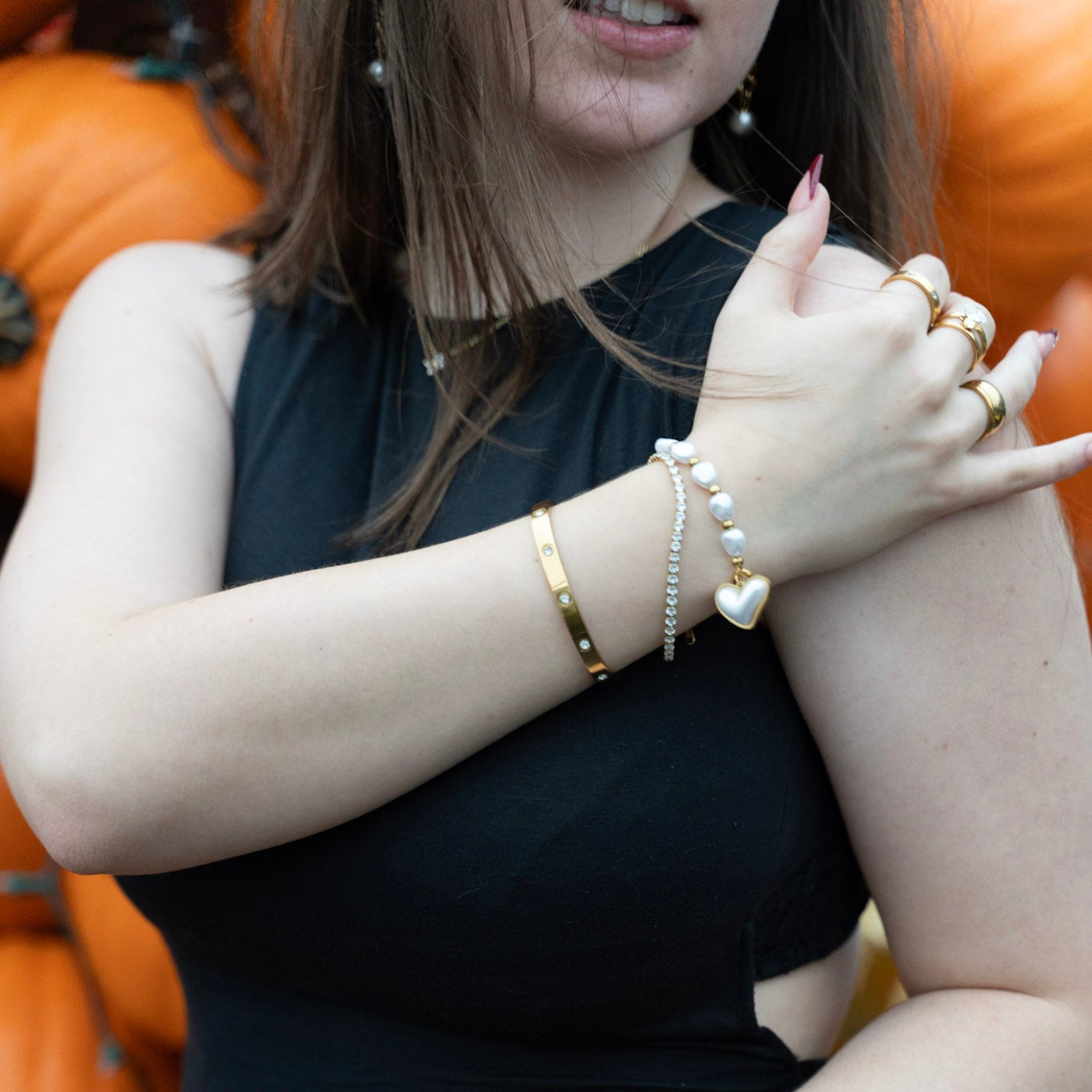 Woman wearing multiple bracelets and rings with a blurred pumpkin patch background