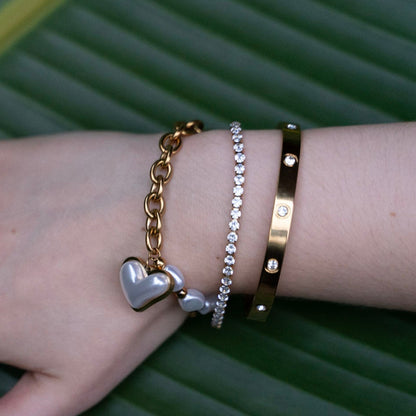 Hand wearing multiple gold bracelets and rings on a green leaf background