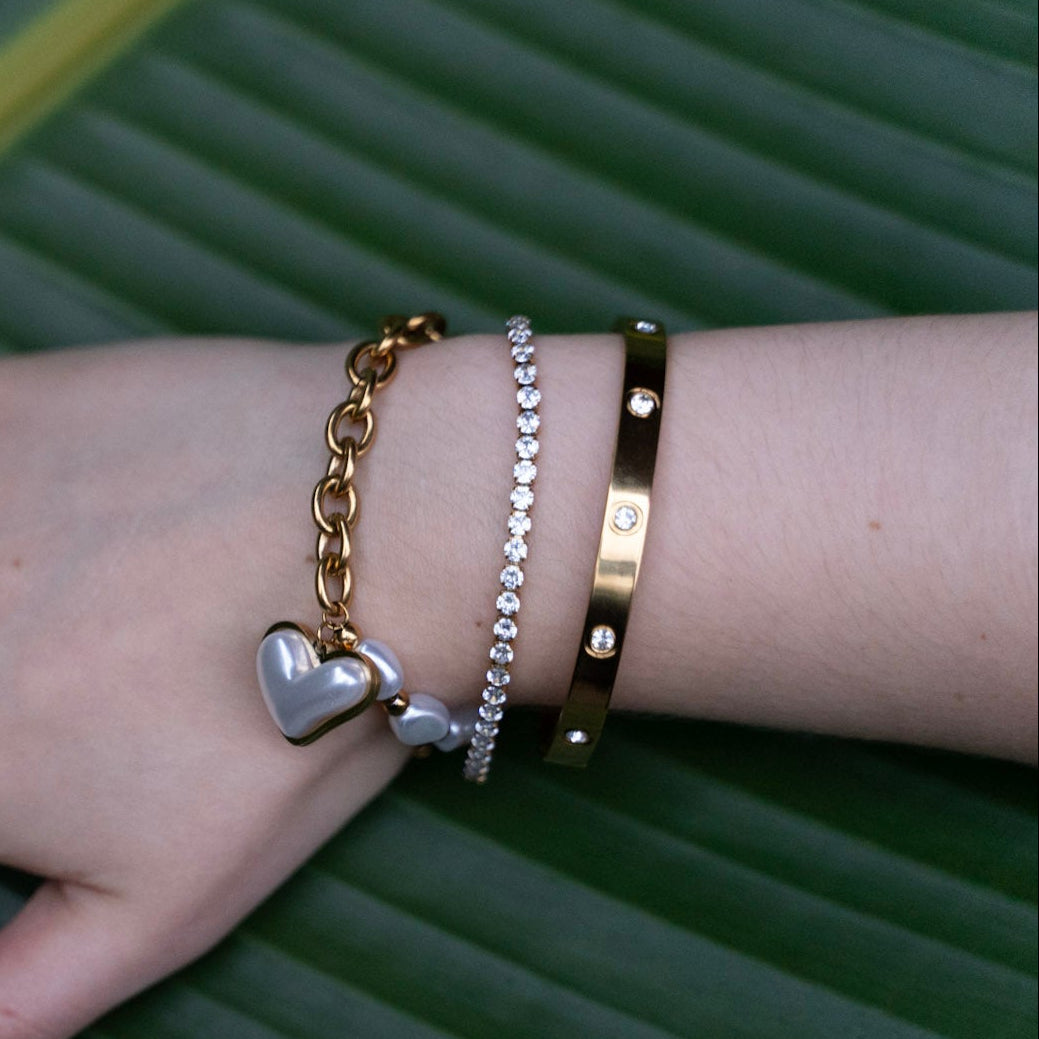 Hand wearing multiple gold bracelets and rings on a green leaf background