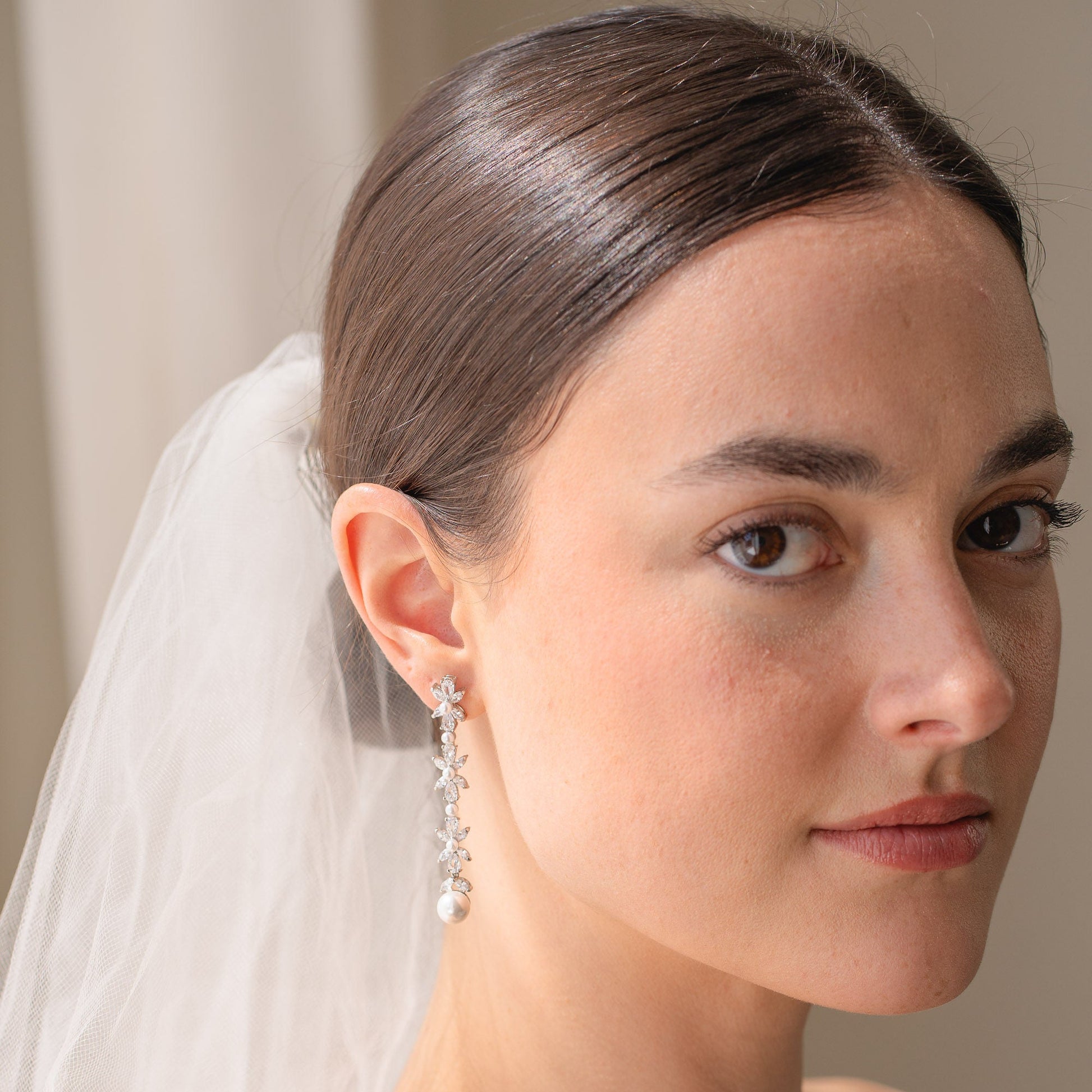 Woman wearing a white veil and earrings against a neutral background