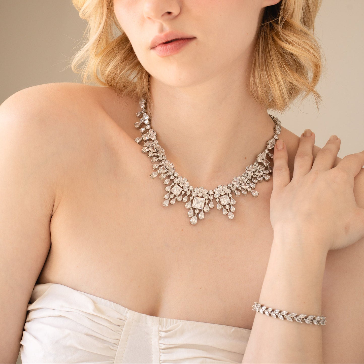 Woman wearing a sparkling necklace and bracelet against a neutral background