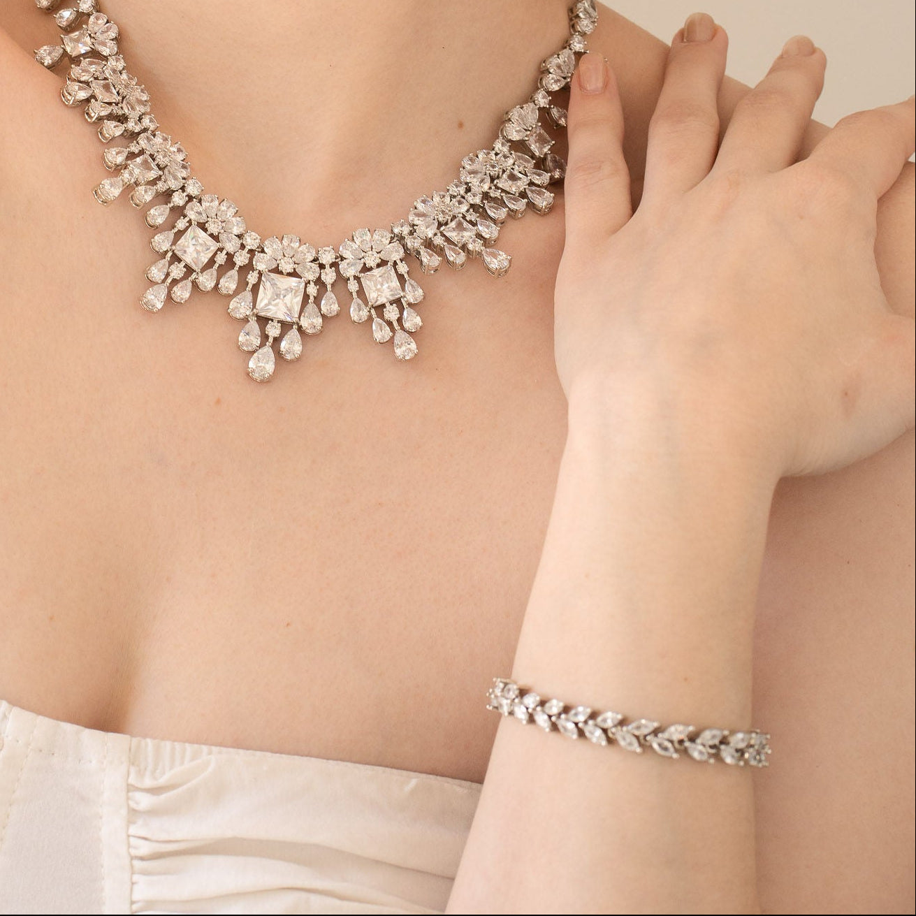 Woman wearing a sparkling necklace and bracelet against a neutral background