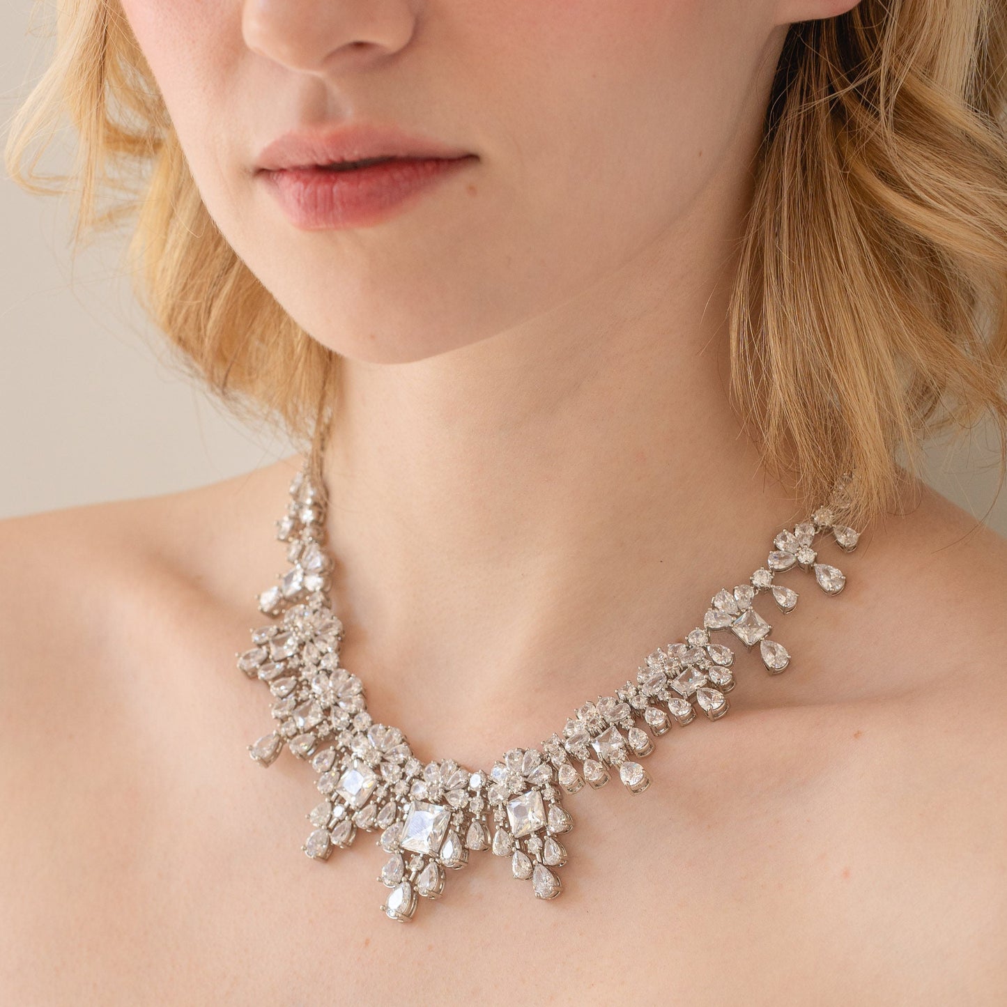 Close-up of a person wearing a sparkling necklace with a neutral background