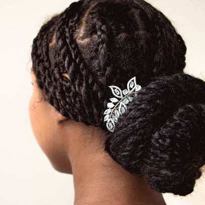 Person with braided hair styled in a bun with a decorative hairpin against a plain background