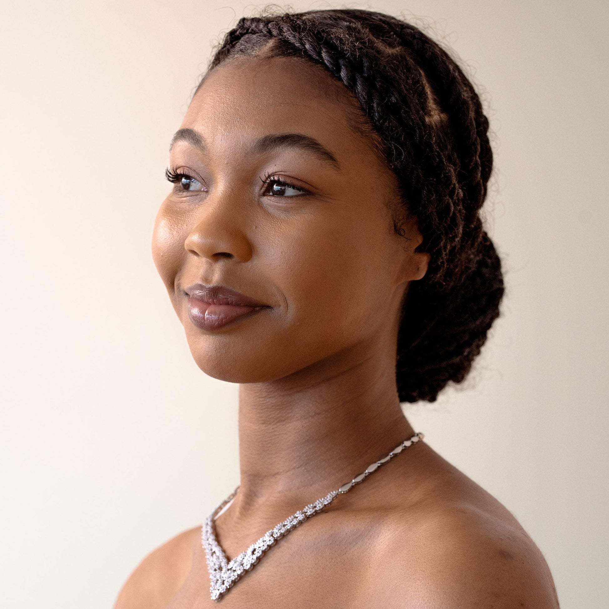 Woman with braided hair wearing a white garment and necklace against a plain background