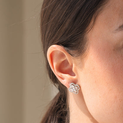 Close-up of a person wearing a silver floral earring with a neutral background