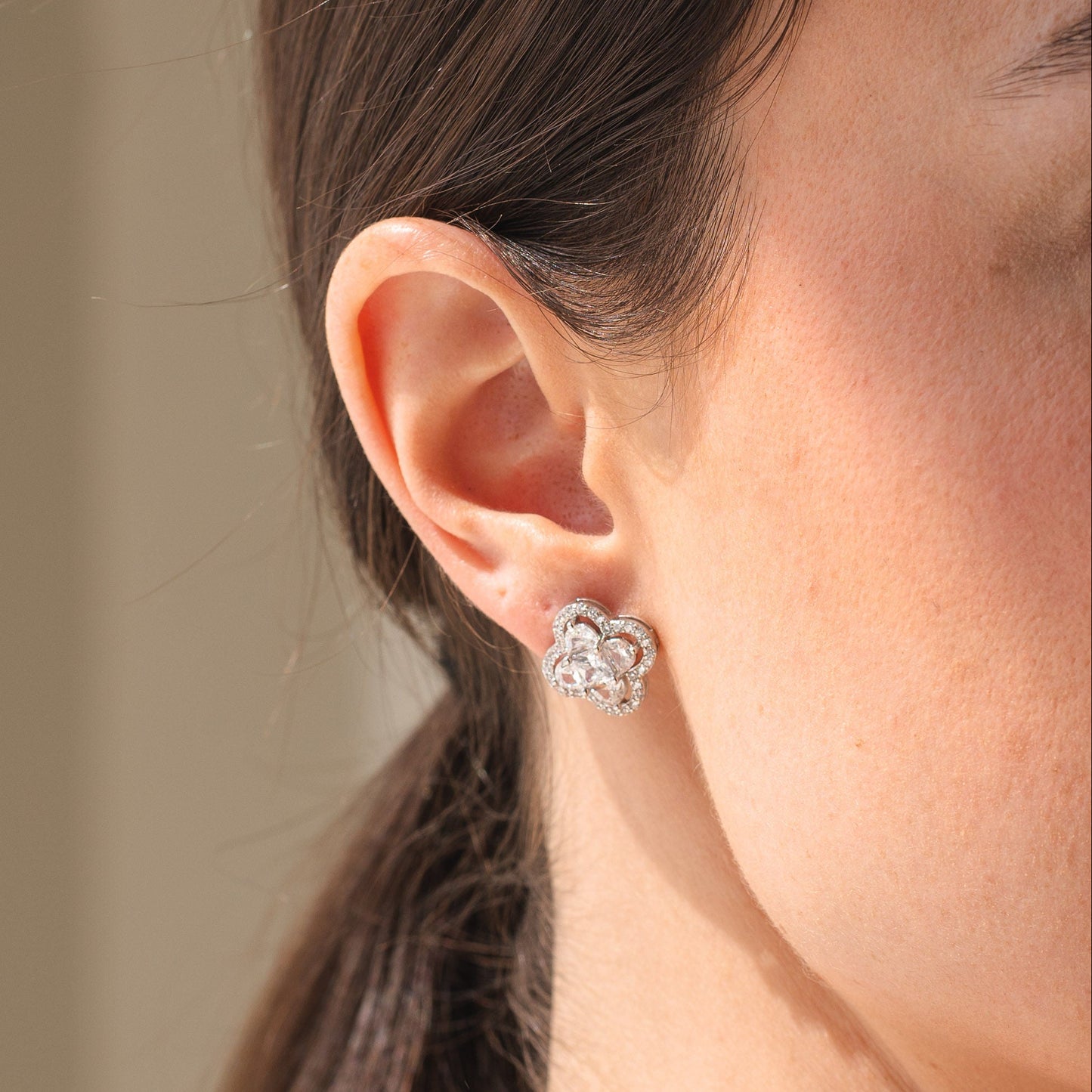 Close-up of a person wearing a silver floral earring with a neutral background