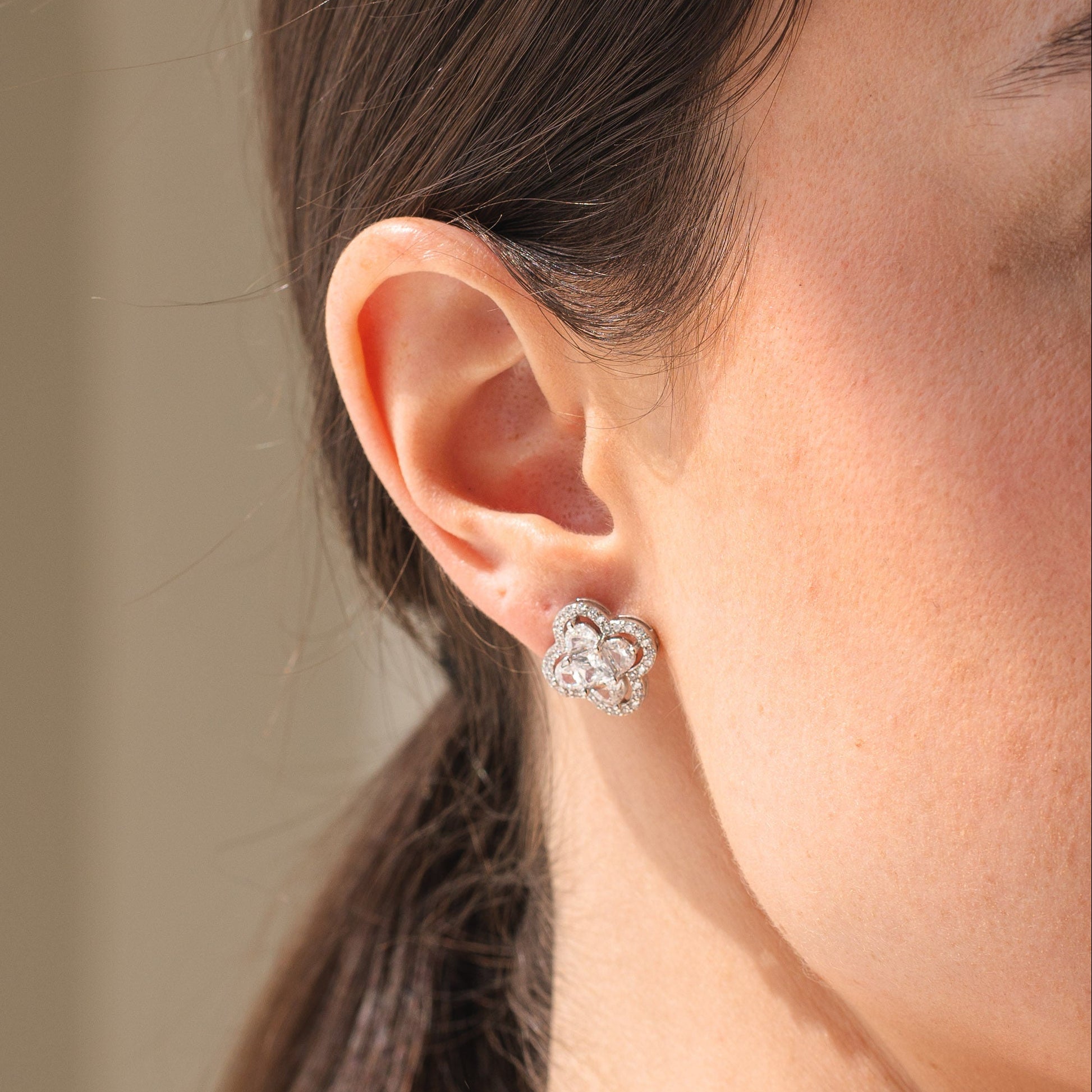 Close-up of a person wearing a silver floral earring with a neutral background