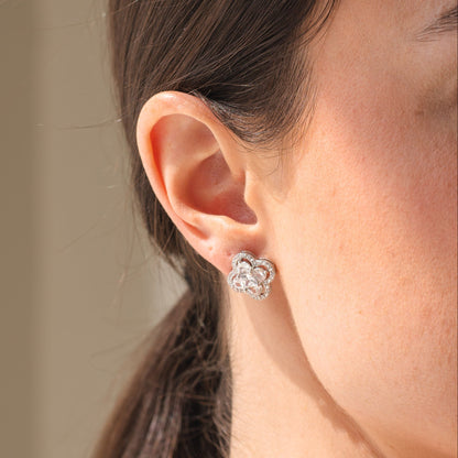 Close-up of a person wearing a silver floral earring with a neutral background