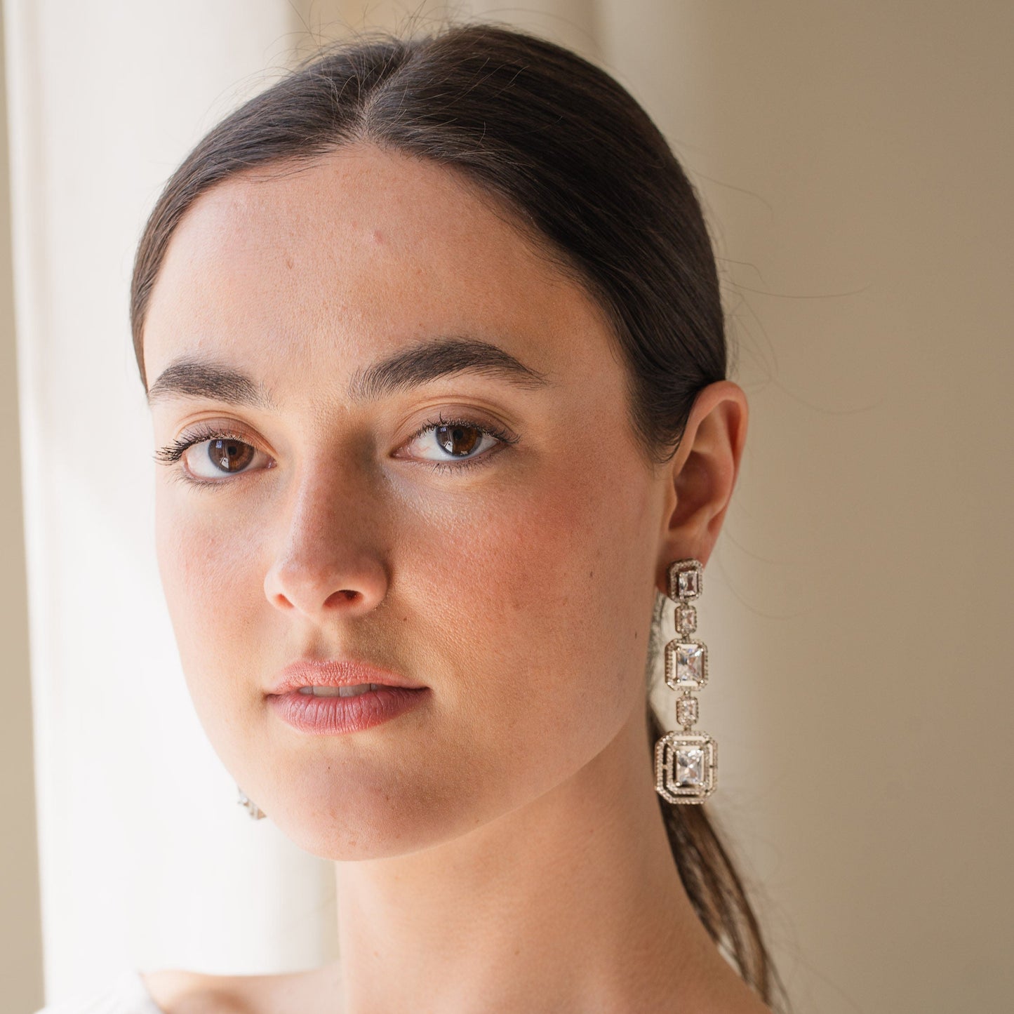 Woman wearing large, ornate earrings indoors with a neutral background