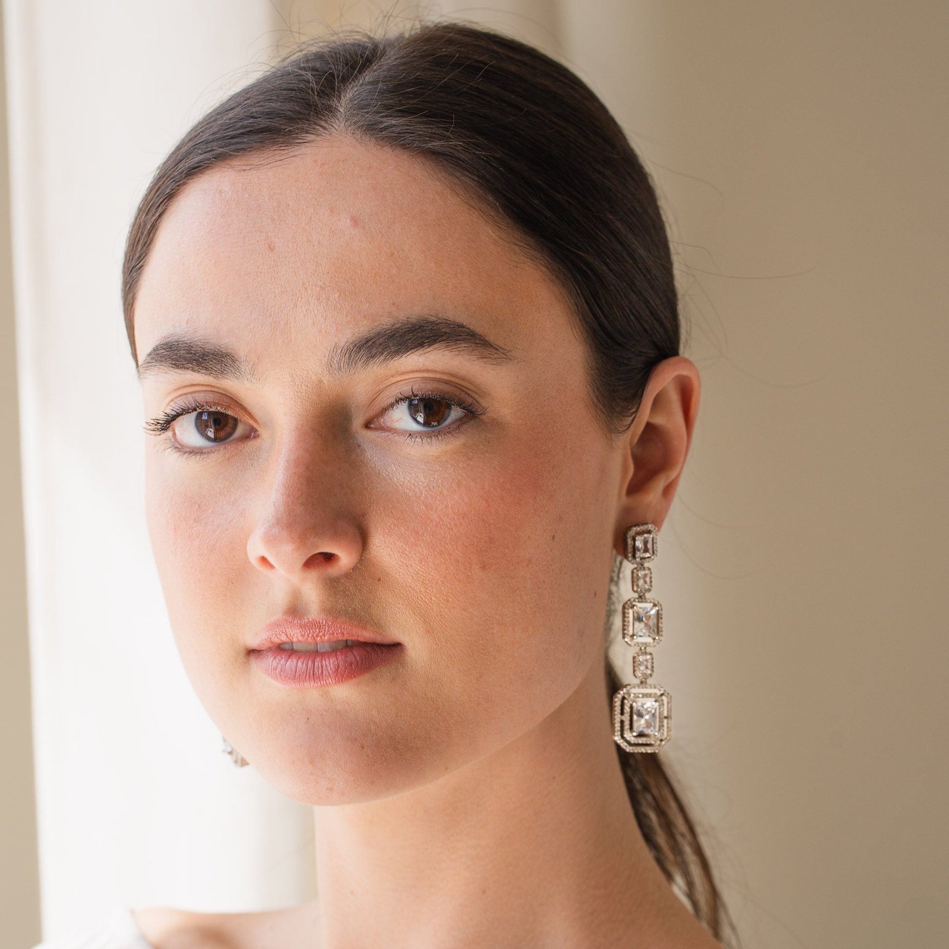Woman wearing large, ornate earrings indoors with a neutral background
