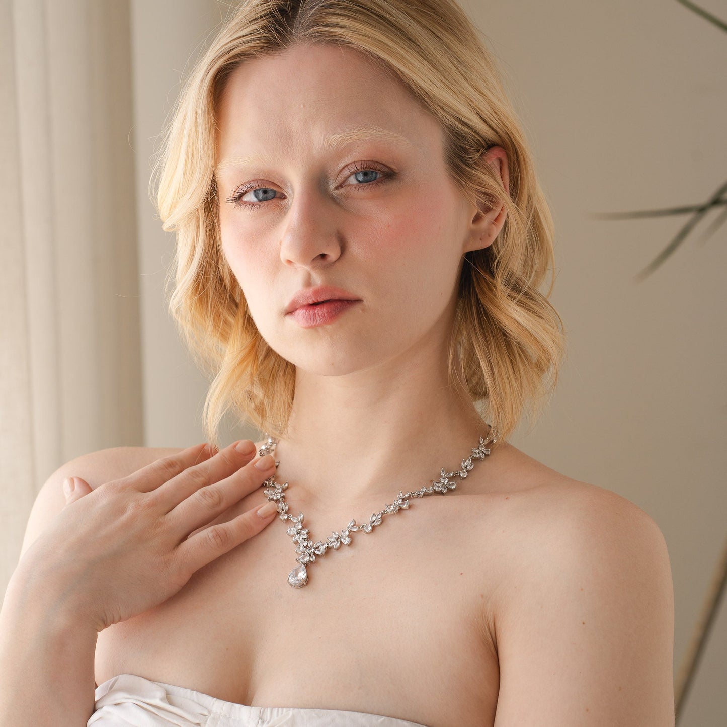 Woman wearing a white strapless dress and a necklace indoors.