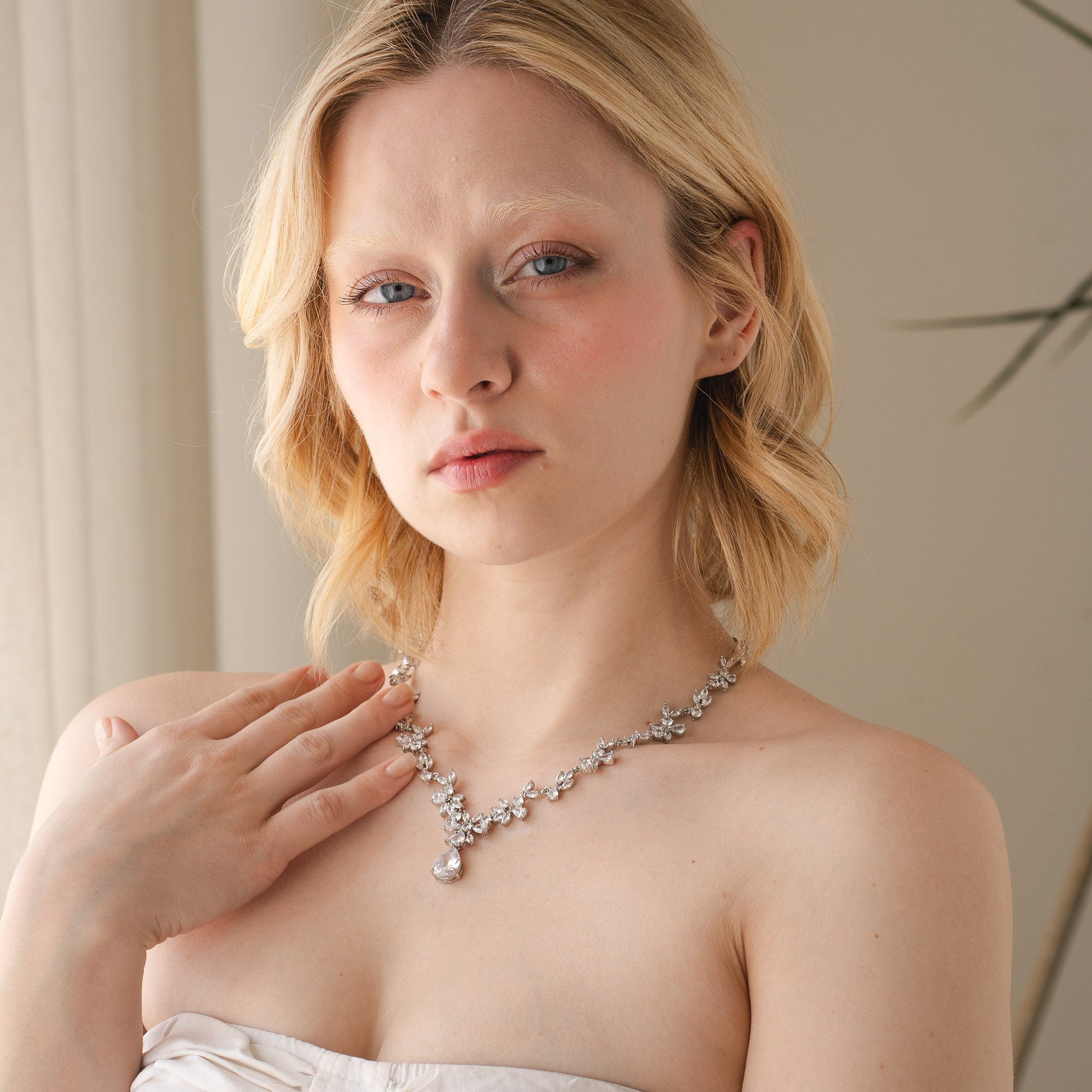 Woman wearing a white strapless dress and a necklace indoors.