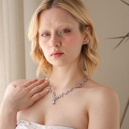 Woman wearing a white strapless dress and a necklace indoors.