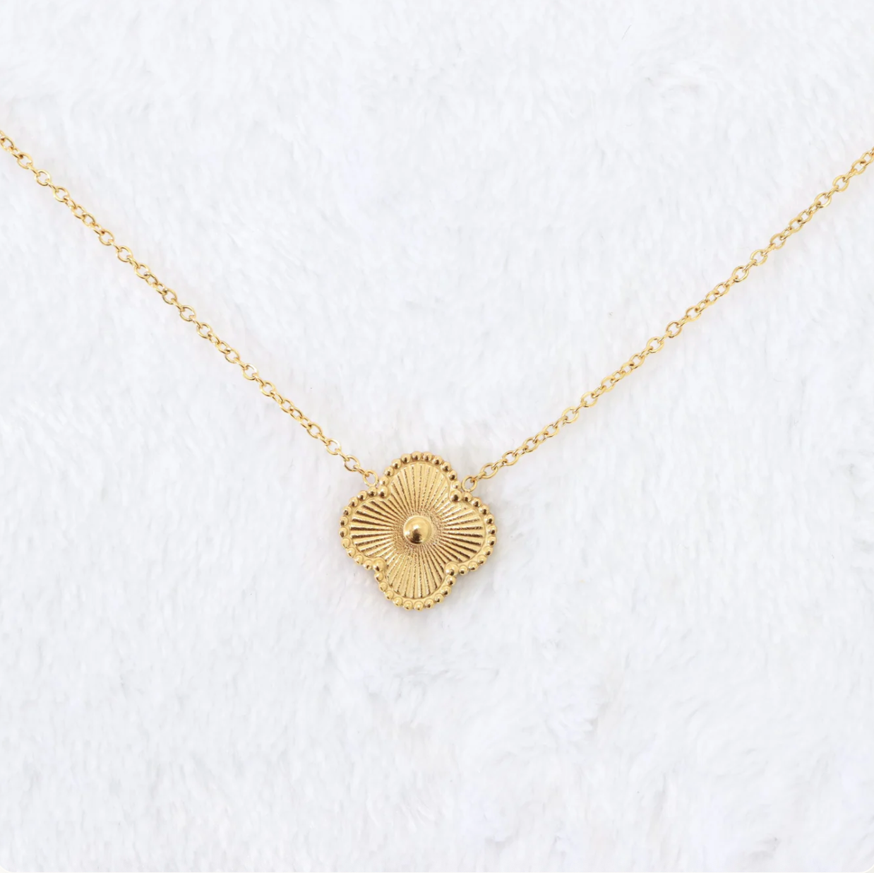 Gold necklace with a circular pendant on a white textured background