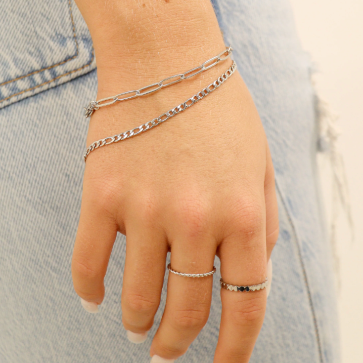 Hand wearing multiple silver bracelets and rings against a denim background