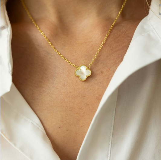 Gold necklace with a clover-shaped pendant worn by a person in a white shirt.